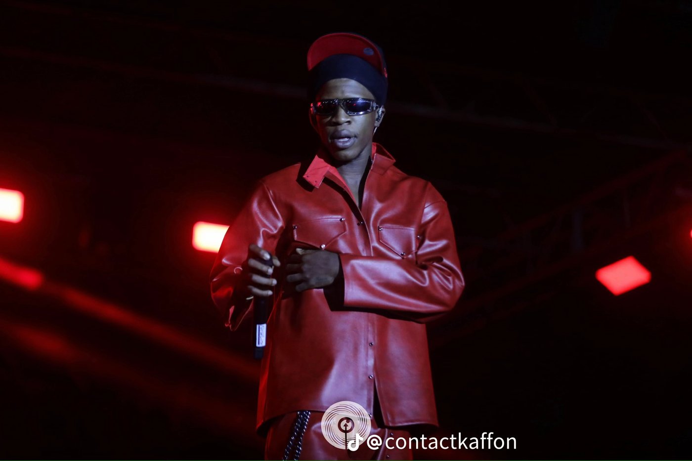 Renard Barakissa, veste orange brillante, casquette, lunettes argent, micro, concert